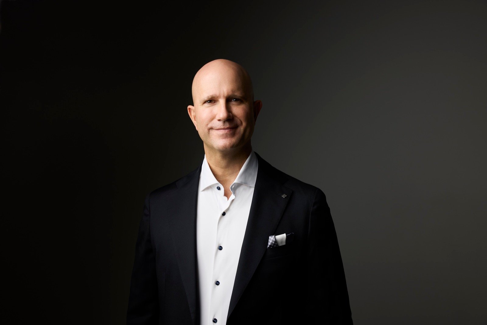 Marvin J. Schmidt in a dark blazer against a charcoal background, speaking-ready portrait.