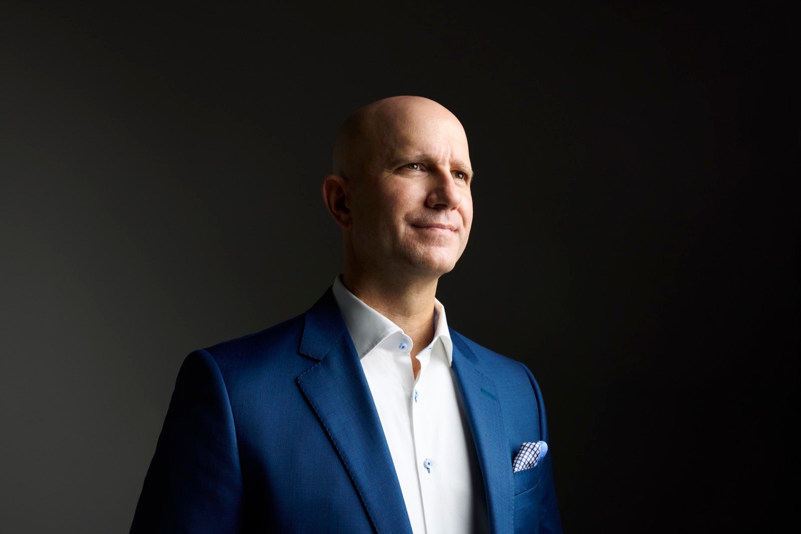 Marvin J. Schmidt, formal editorial portrait in a dark suit against a charcoal background.